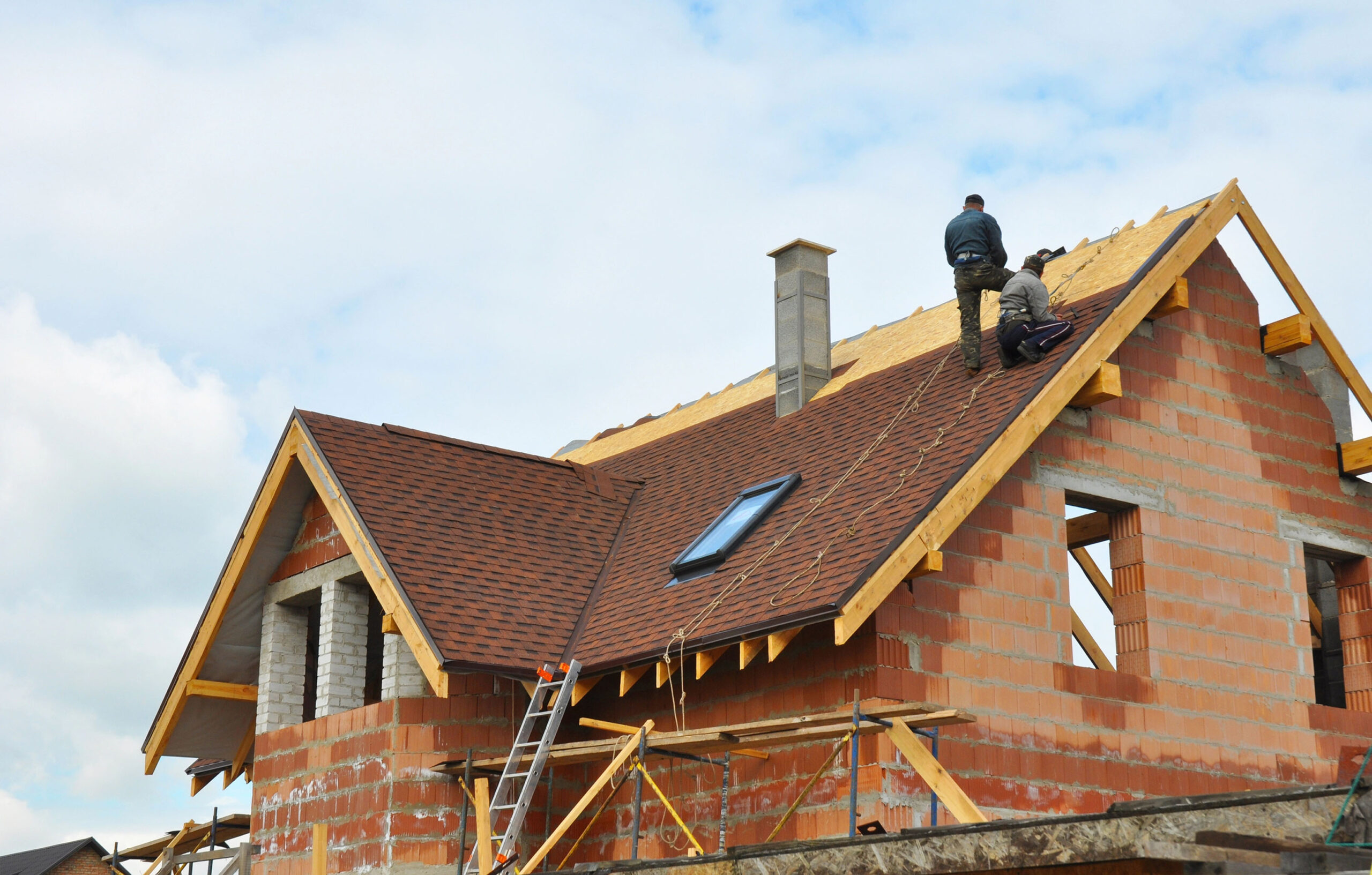 Dachdecker bei der Montage von Bitumenschindeln auf einem Neubau-Einfamilienhaus mit Sichtmauerwerk
